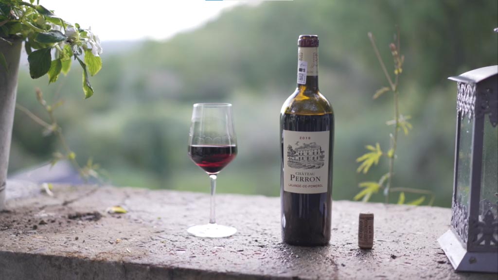 Bouteille Château Perron 2018 débouchée, avec un verre de vin servi.